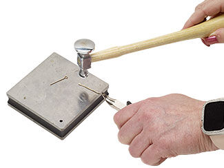 hands hammering a piece of wire on a steel block